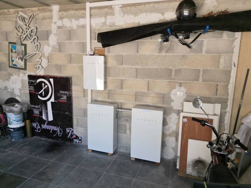 Deux batteries de stockage Atmoce installées dans un garage, complétant un système solaire avec des panneaux photovoltaïques visibles sur le toit pour l'autoconsommation énergétique.
